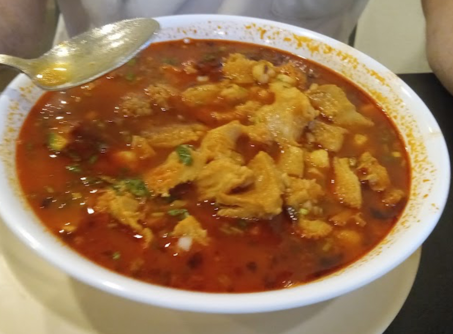 Bowl of red menudo with cilantro and onion
